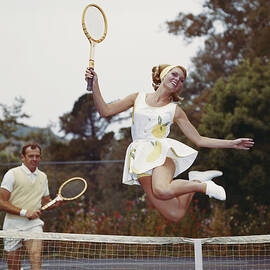 Couple On Tennis Court, Woman Jumping by Tom Kelley Archive